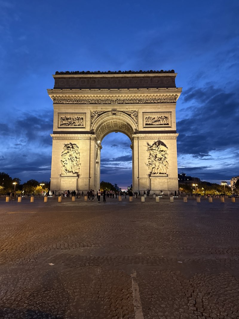 The Arc de Triomphe lit up at dusk under a blue evening sky