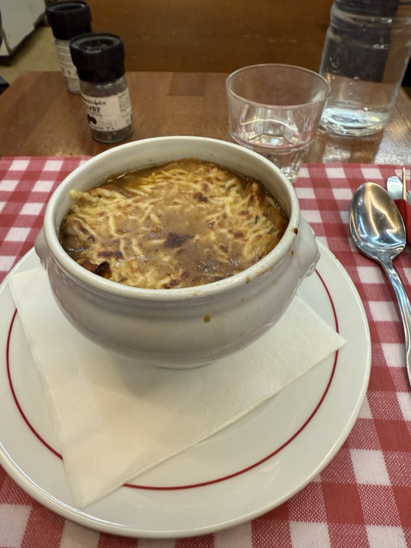 French onion soup with melted cheese on a red-checked tablecloth at Le Petit Vendôme