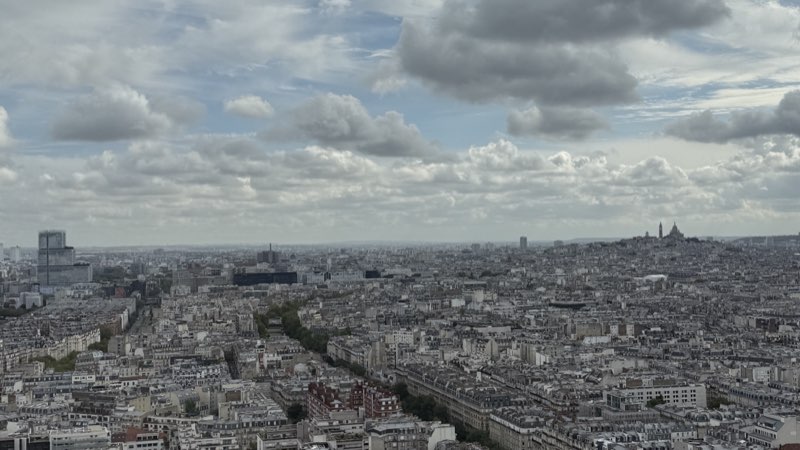Paris rooftops under a cloudy sky, with Sacré-Cœur on the horizon